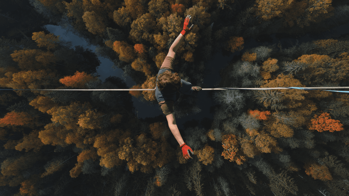 person balancing on a tightrope high above a forest, representing the precision of navigating vulnerability management.